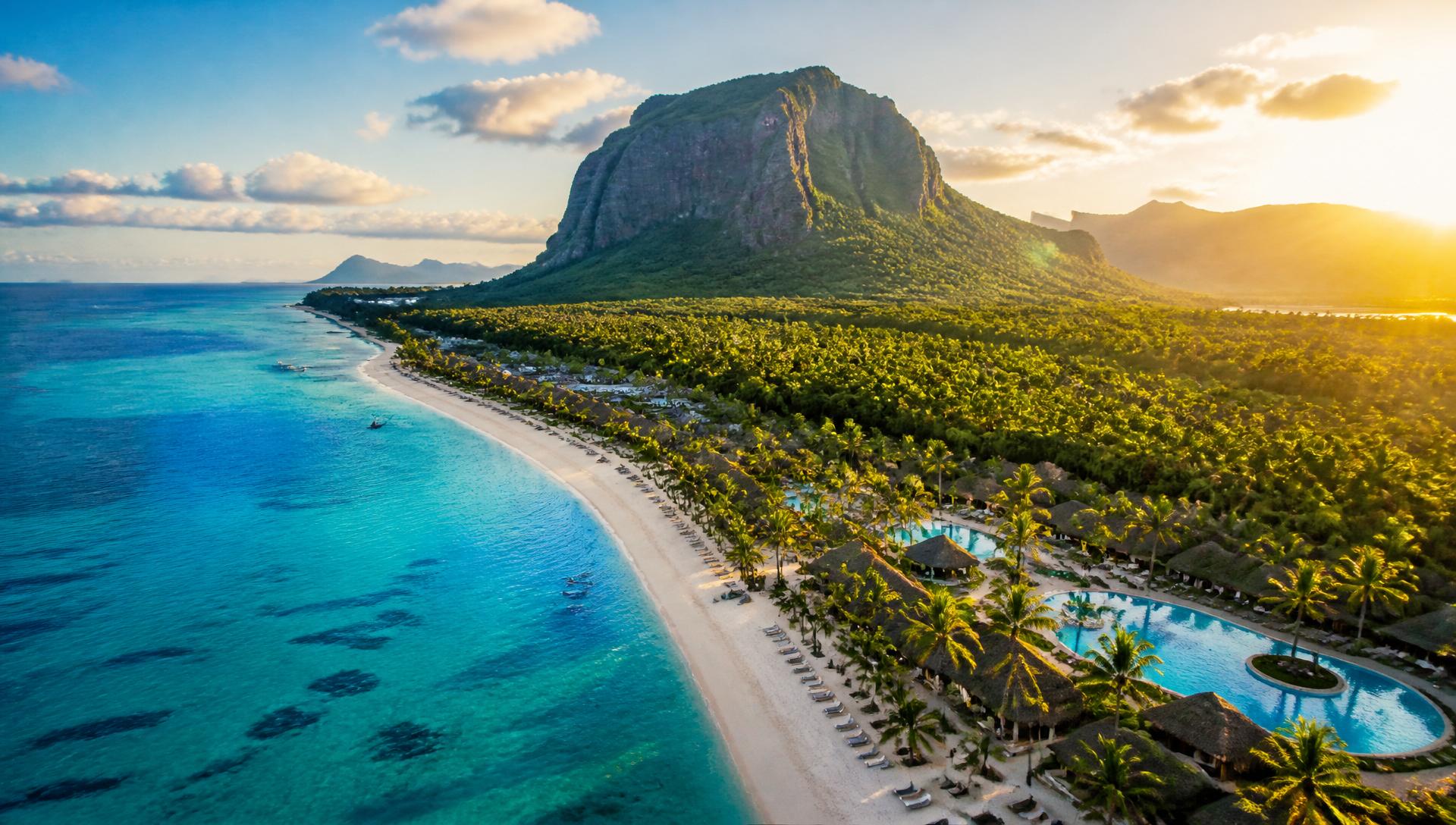 Aerial view of a curving white-sand beach and turquoise lagoon in Mauritius with Le Morne Brabant mountain in the background at golden hour